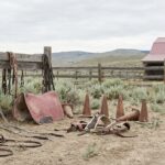 various horse training equipment, including bridles, saddle pads, and cones, on a dusty rural ground near a barn.