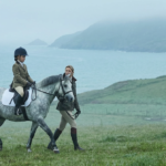 young girl on a horse with an instructor during her first riding lesson by the sea